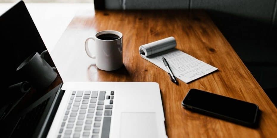 wooden table with notepad, computer, and coffee